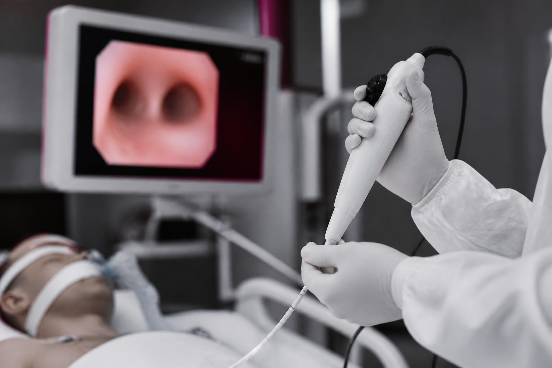 Clinician at an ICU bedside holding a single-use flexible bronchoscope with an airway image on the monitor